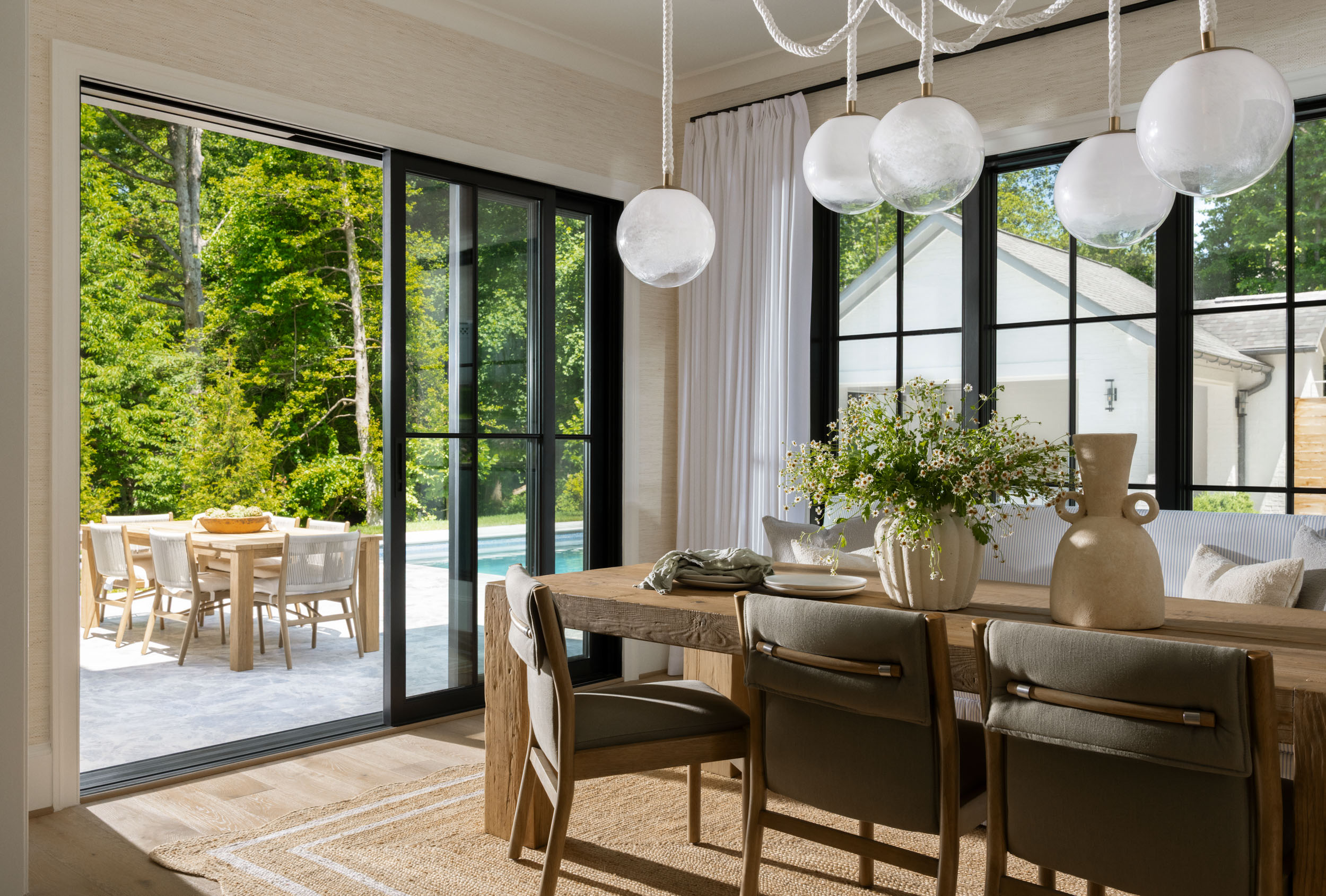 Dining room with a reclaimed oak table, glass globes hung on rope cords, and sliding doors open to the pool terrace