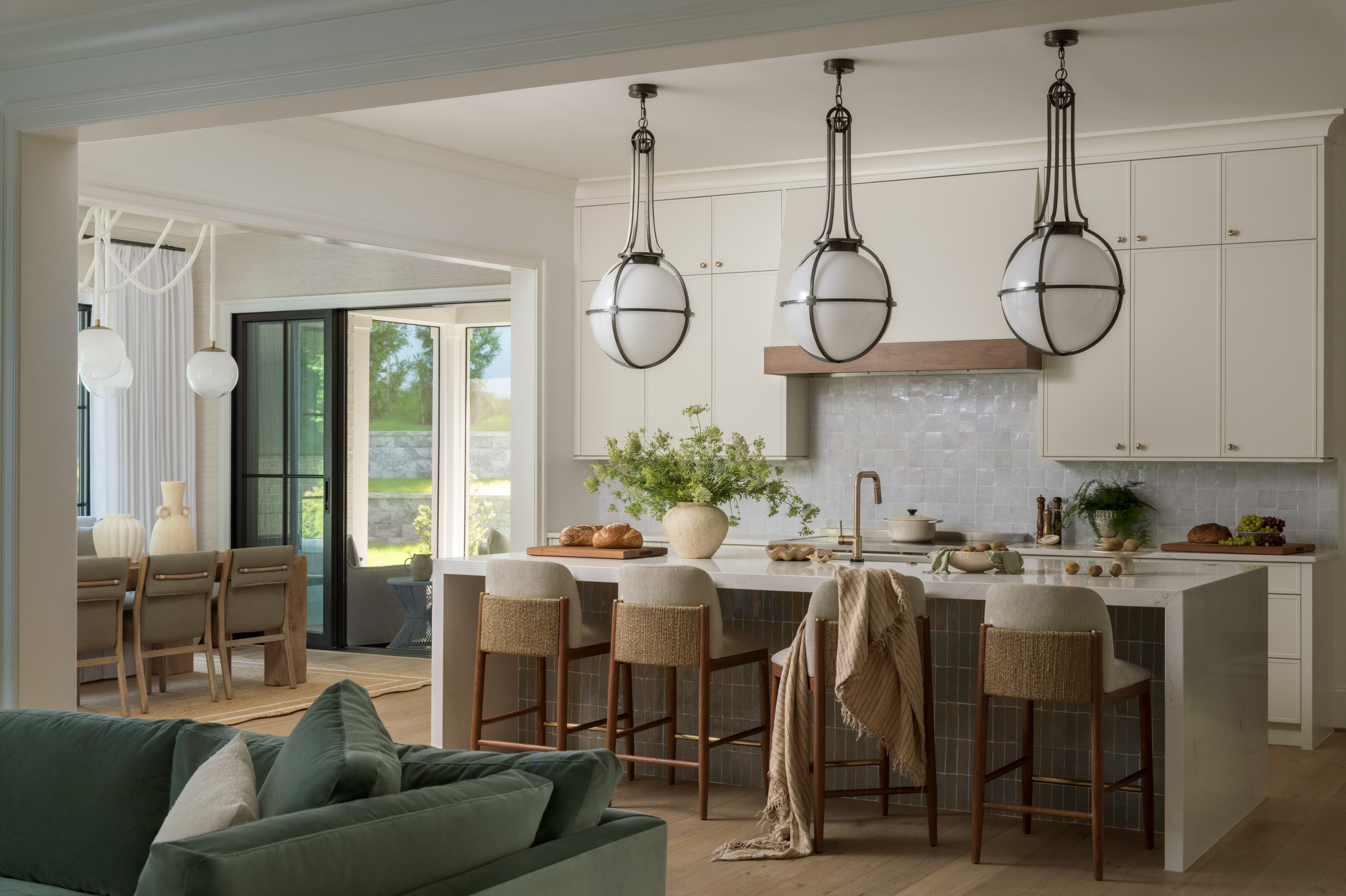 Open kitchen with globe pendants over a zellige-tiled island, woven counter stools, and a dining nook beyond